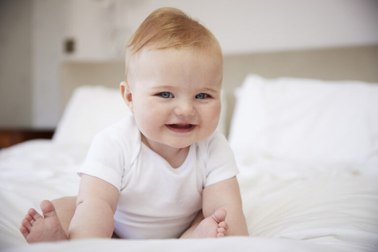 Smiling Baby Trying to Sit Up on Bed