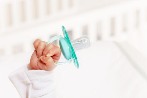 infant hand holding pacifier in crib