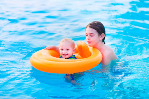 a baby in a baby float for the pool being assisted by his older brother