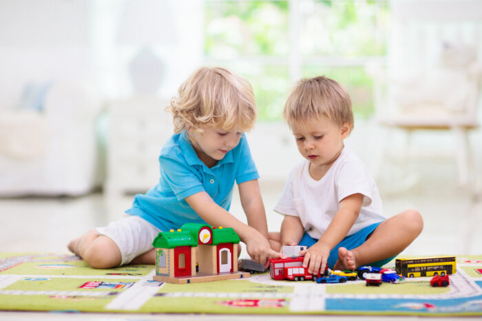 two young boys playing with toys on a carpet playmat