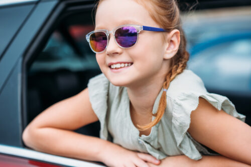 little girl wearing kids sunglasses leaning out of car window and smiling