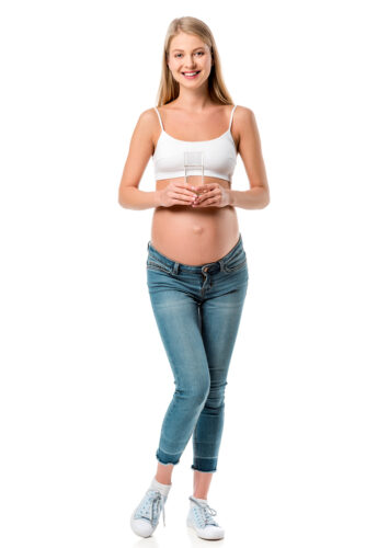 studio shot of pregnant woman in white tank top and jeans against white background