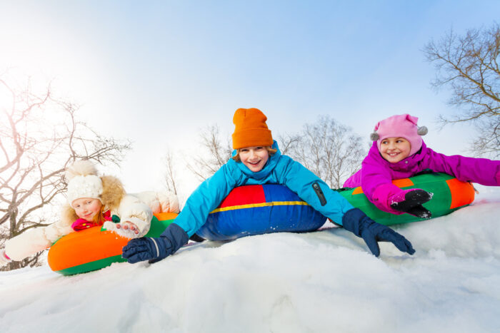 children sliding down a snowy hill on sleds