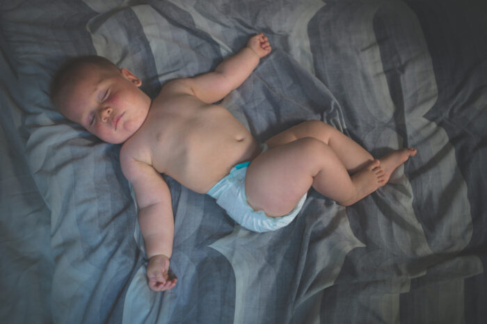 A cute little baby in his diaper is sleeping on a bed