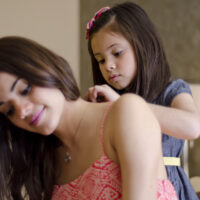 young girl putting a necklace on her mom