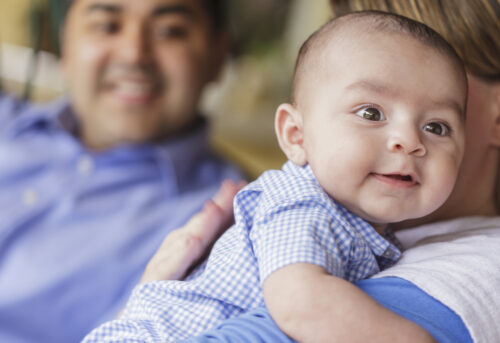 smiling father talking to mother while she burps their cute infant son