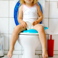 Toddler girl sitting on the toilet and grabbing toilet paper