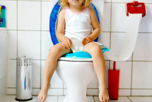 Toddler girl sitting on the toilet and grabbing toilet paper