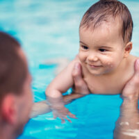 smiling baby boy being held by parent in pool