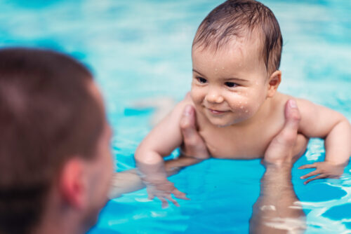smiling baby boy being held by parent in pool