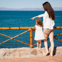 single mother and her daughter looking at the ocean view from a balcony