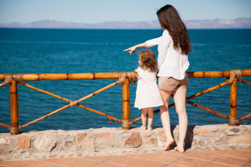 single mother and her daughter looking at the ocean view from a balcony