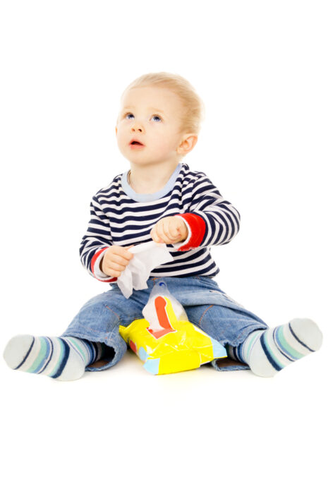 young toddler boy playing with a package of baby wipes against a white background