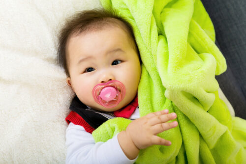 baby holding blanket with pacifier in his mouth