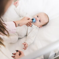 mom giving her young baby a pacifier in the crib