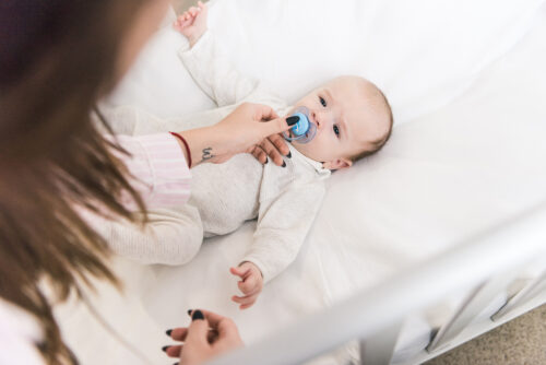 mom giving her young baby a pacifier in the crib