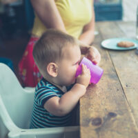 mom helping her baby to drink from an open cup