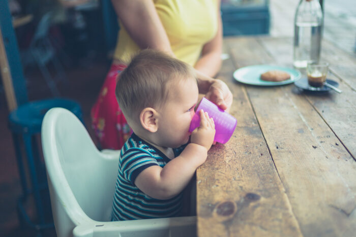 mom helping her baby to drink from an open cup