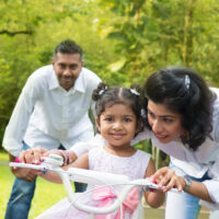 family teaching daughter how to ride a bike