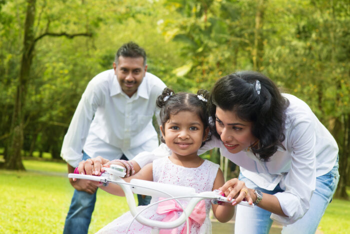 family teaching daughter how to ride a bike